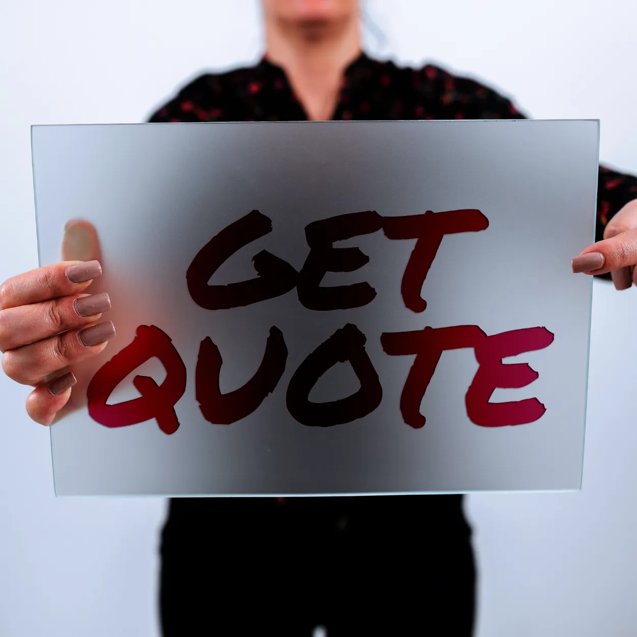 A person holds a translucent sign that reads “GET QUOTE” in bold, dark red letters.